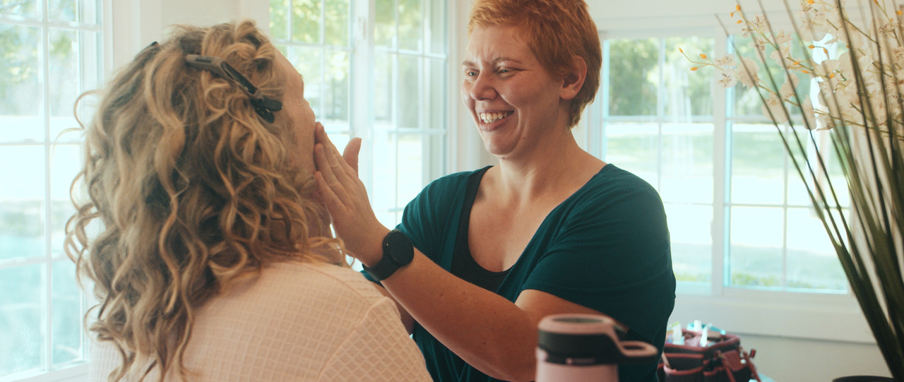 Makeup artist smiles at bride as she applies makeup.