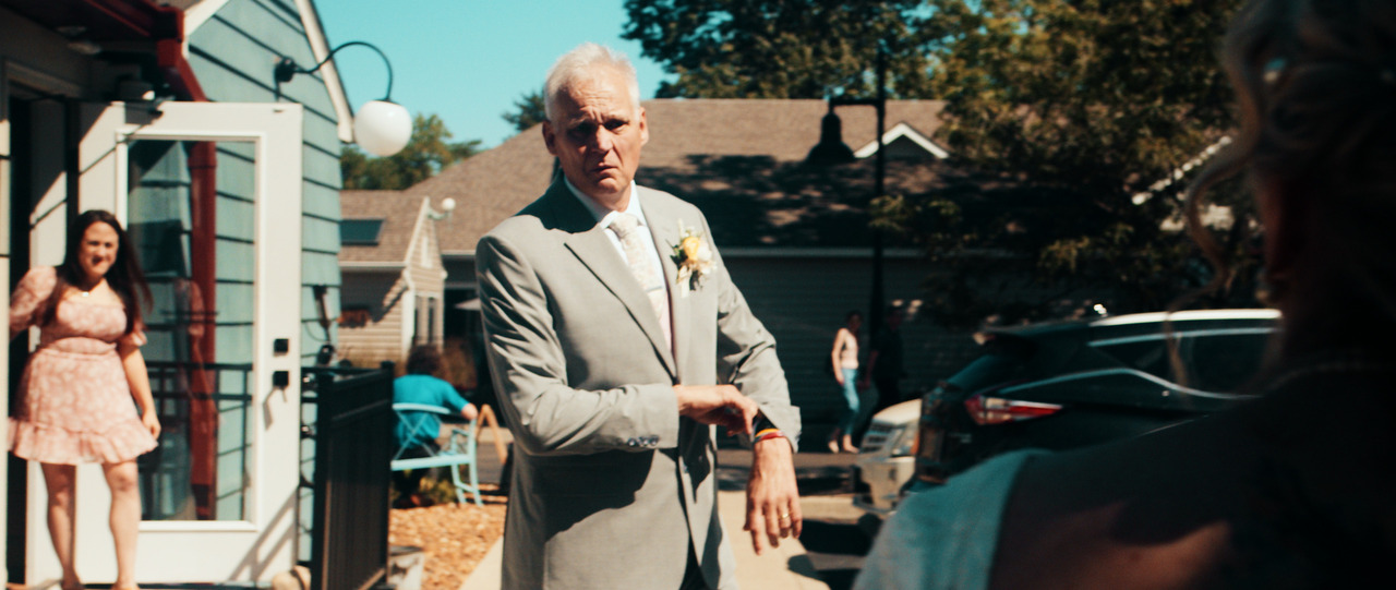 Groom checks watch outside reception area, looks at camera.