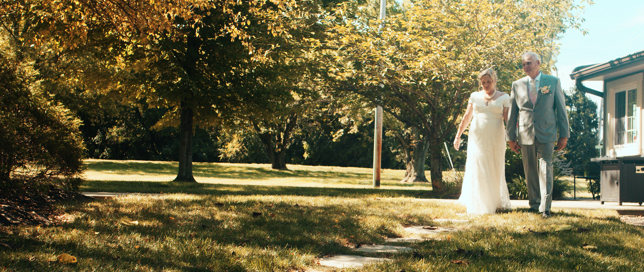 Bride and groom walk together down forest path.