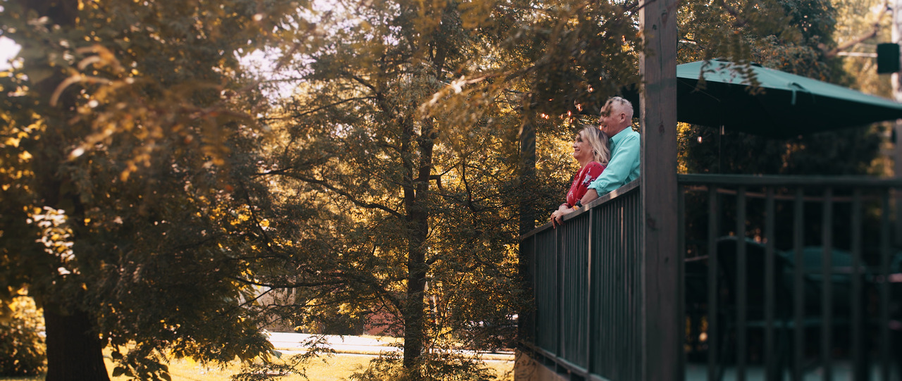 Groom holding bride as they stare out from porch.