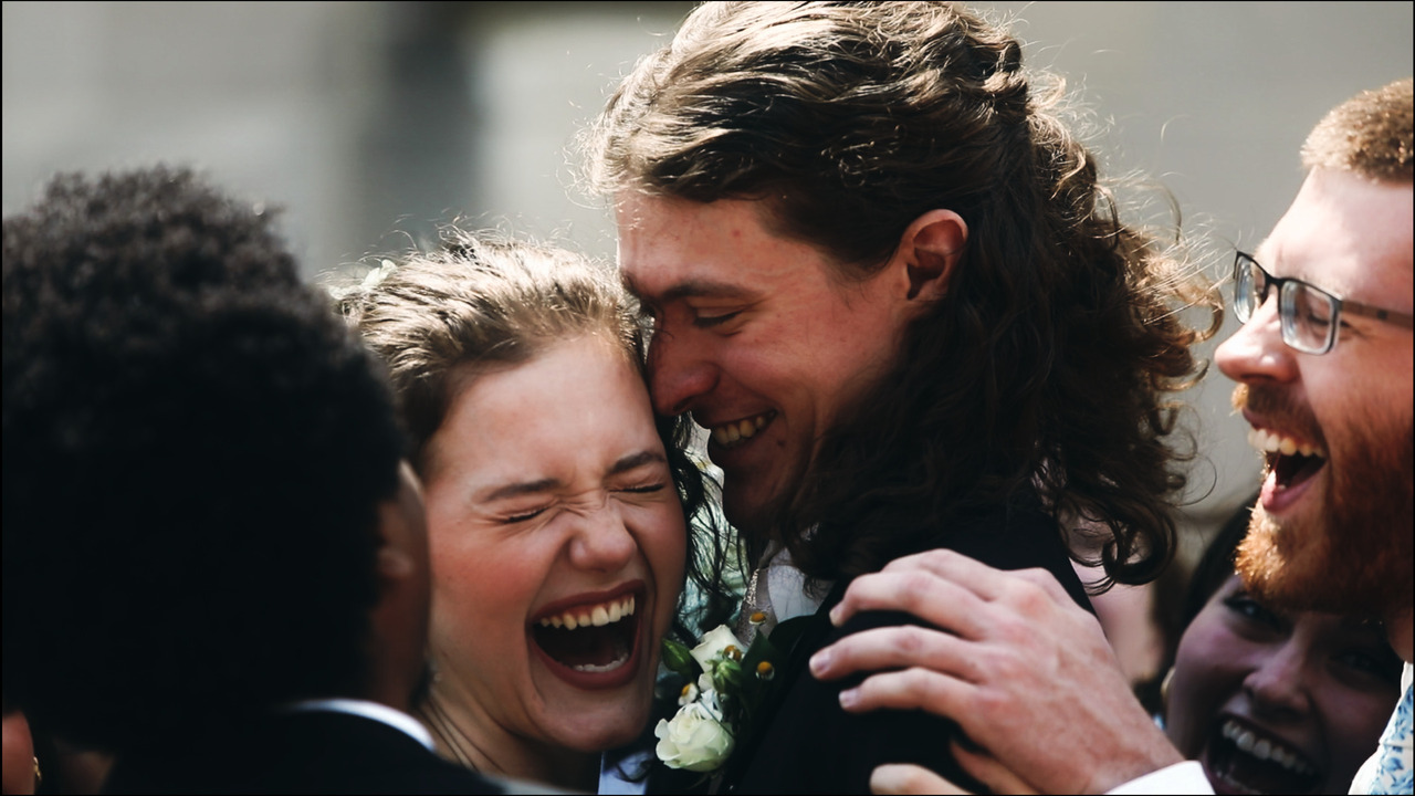 Bride and groom laughing while being hugged by bridal party.