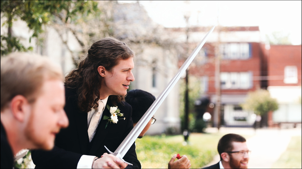 Groom branding sword while groomsmen brandish pocket knives.
