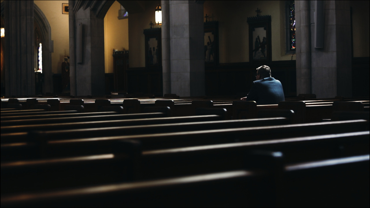 Man praying in pew in dark church.