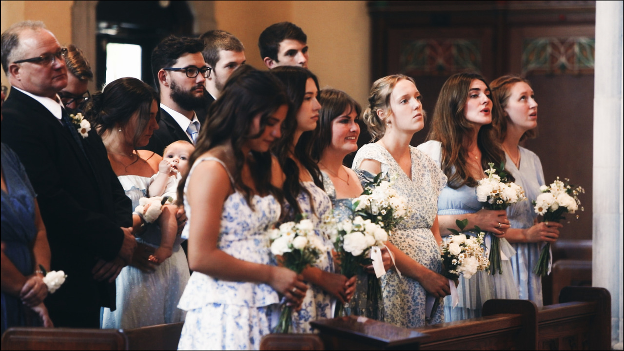 Bridesmaids standing in front pew, watching wedding mass.