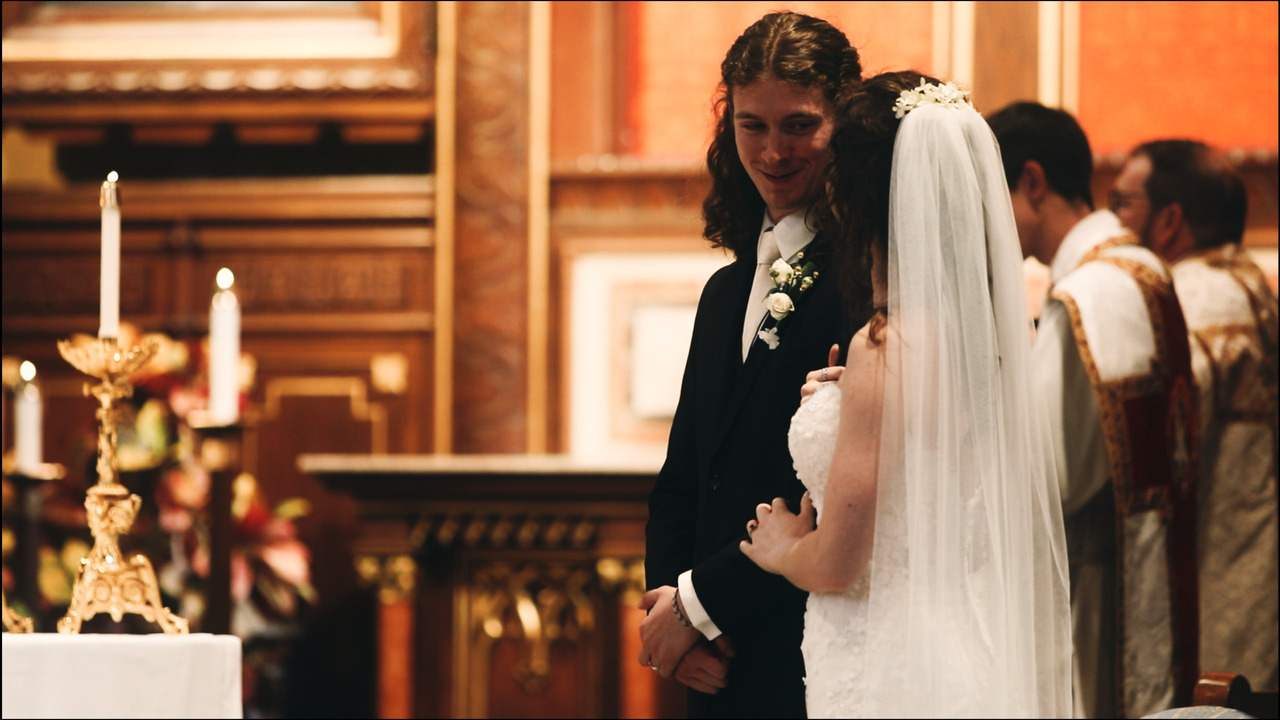 Groom smiling at bride while they stand to side of altar.