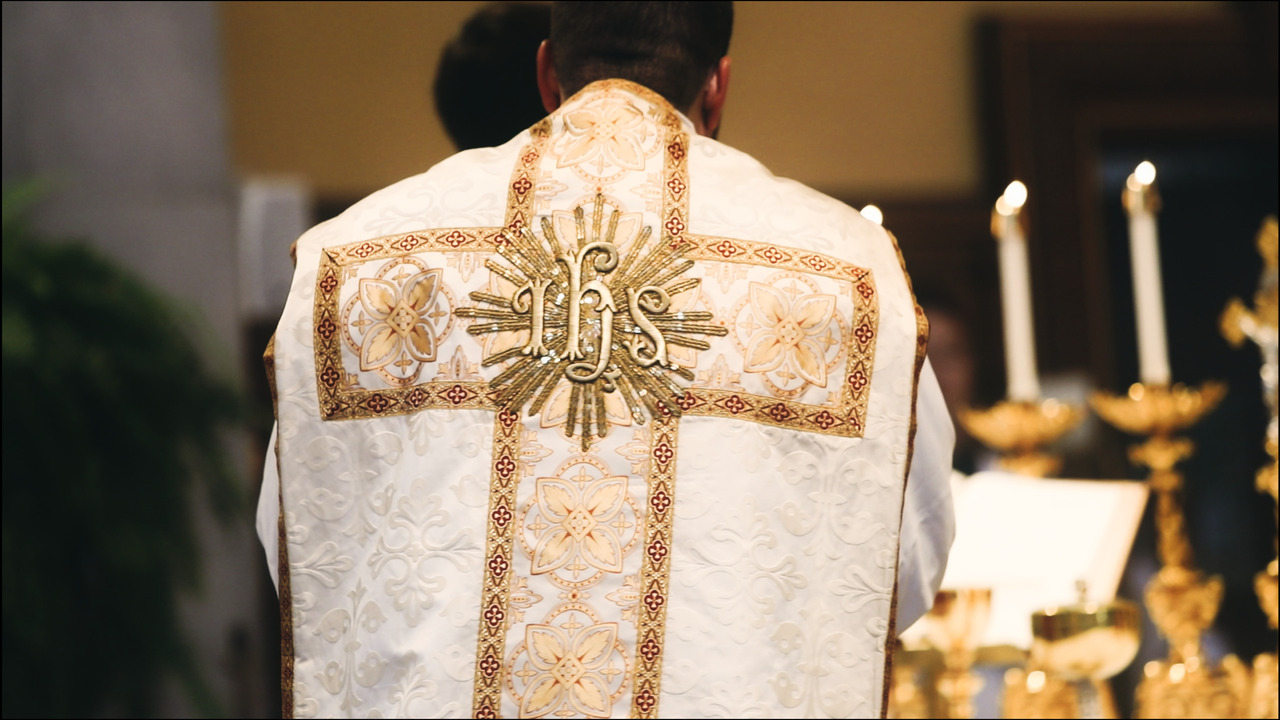 Priest vestment glitters in the light while he assists in the mass.