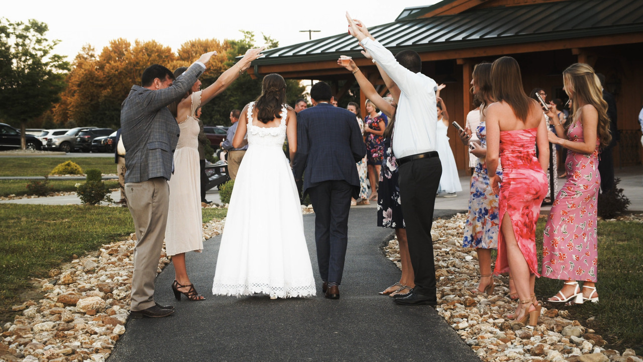 Bride and groom walking under guest arm-tunnel at reception.