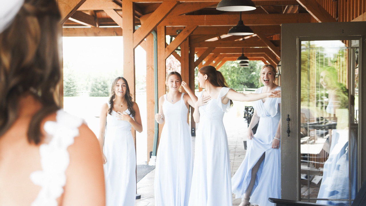 Bridesmaids gasp and smile at bride's dress (first look).