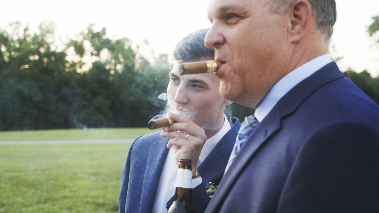 Groom and older man smoke ciguars together.