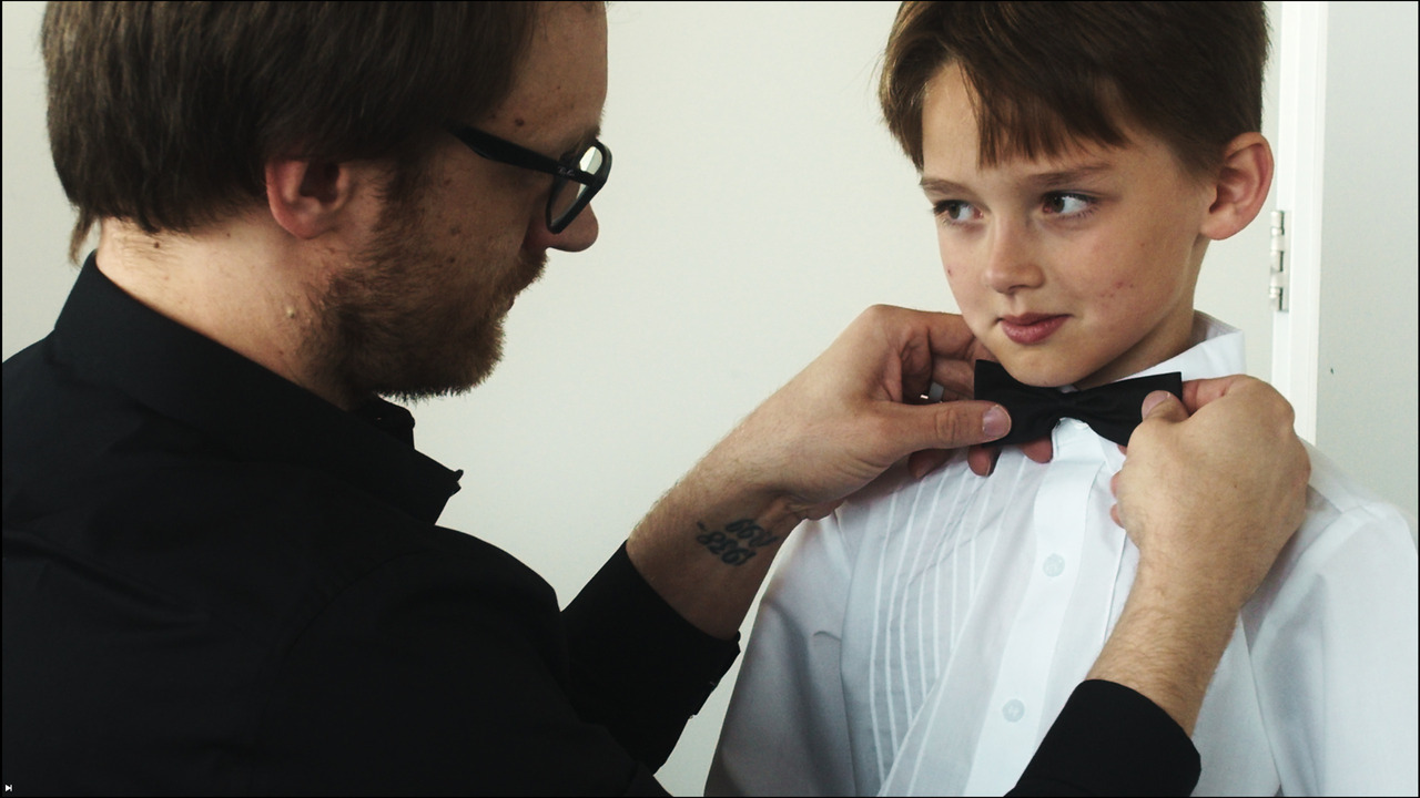 Groomsmen puts bowtie on boy.