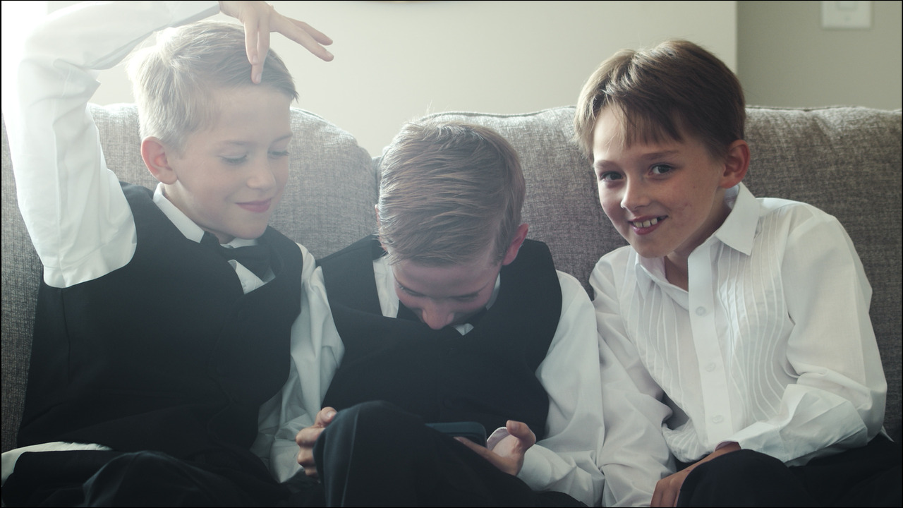 boys in dress shirts and vests mess around on couch.