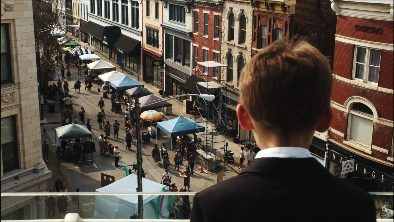 boy looks out over balcony to street with festival tents.