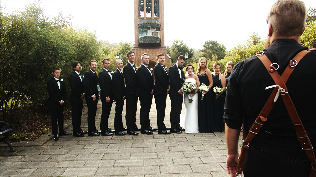 Photographer prepares to take photo of bridal party, with bride and groom in center.