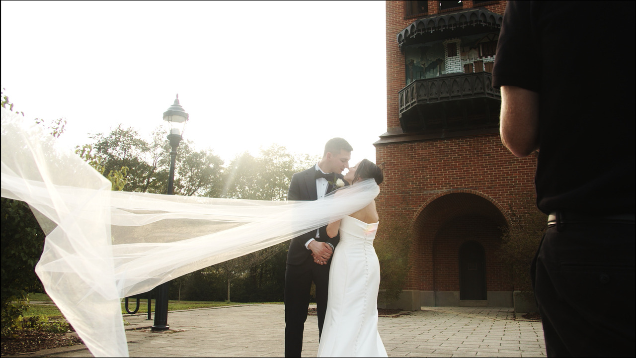 Bride and groom nuzzle while her veil flows in wind.