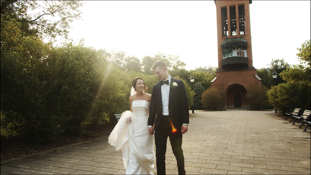 Bride and groom walk together with sun in background.