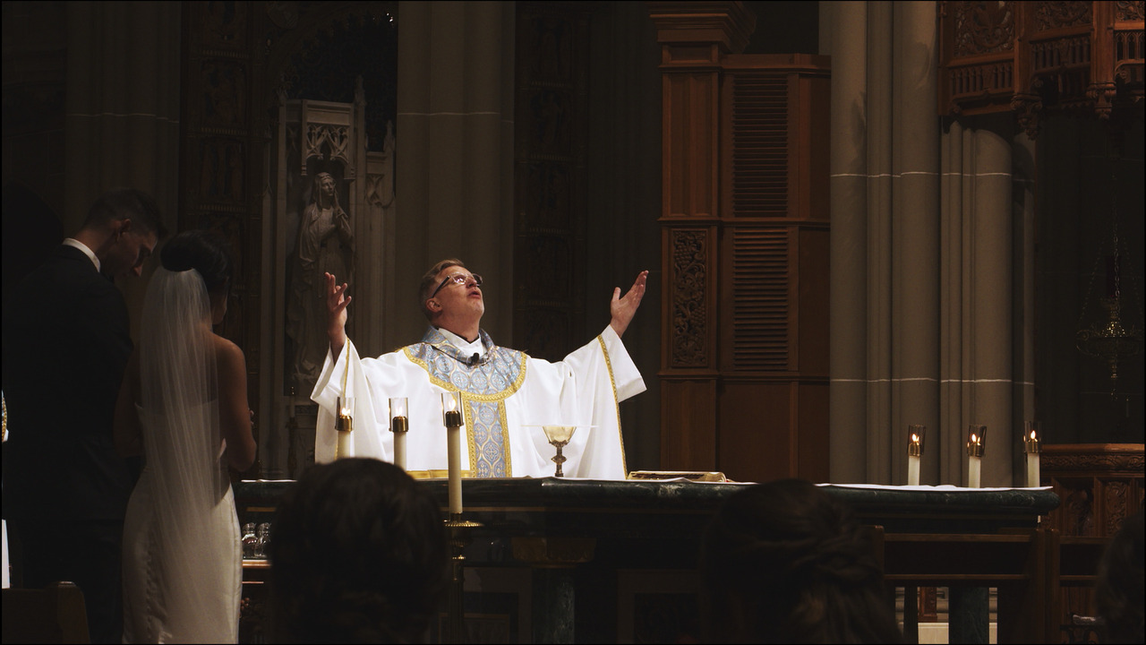 Priest holding up his arms and praying behing altar.