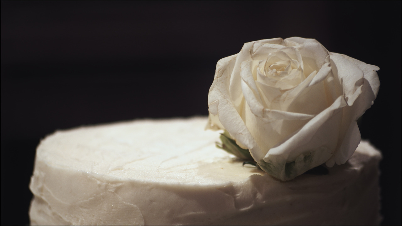 Closeup of white rose placed on top of wedding cake.