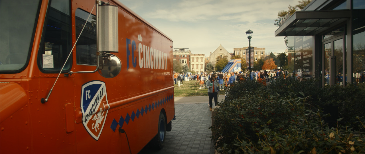 Orange FC Cincinnati van, with tailgate in the park in the background.
