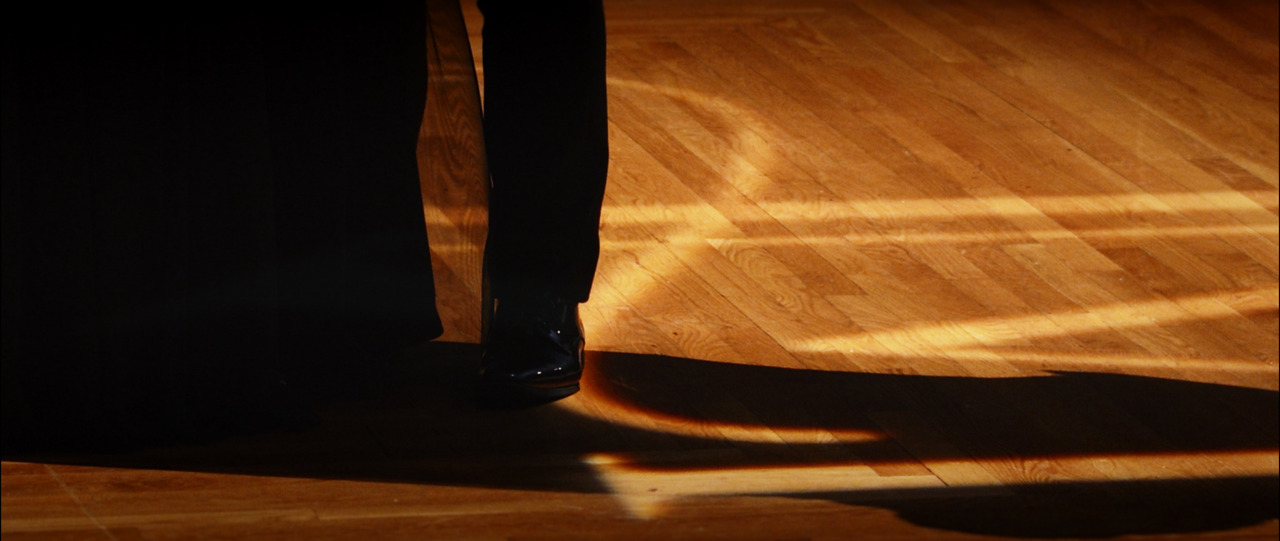 Closeup of a black dress shoe and projected 'JM' logo on floor.