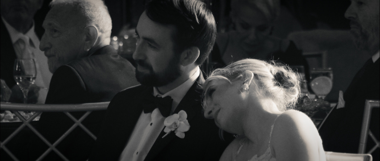 Bride resting her head on groom's shoulder as they listen to toasts.