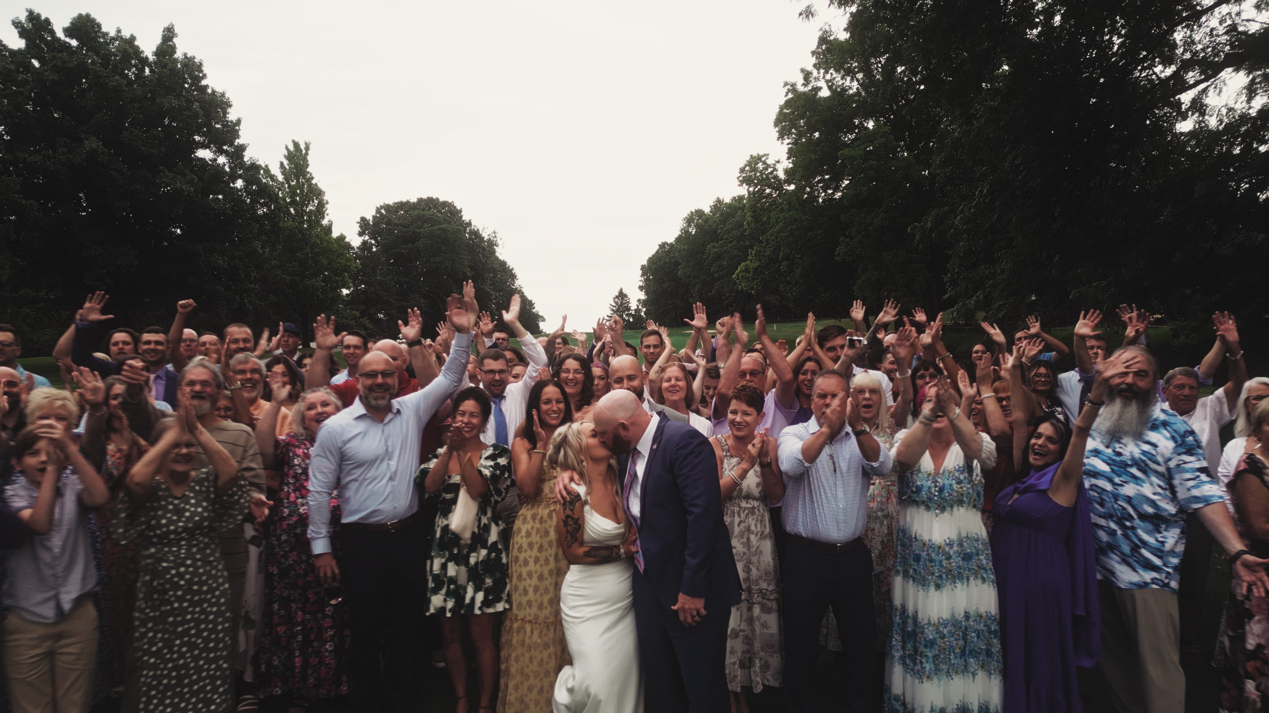 Couple kissing on golf course, surrounded by guests cheering.