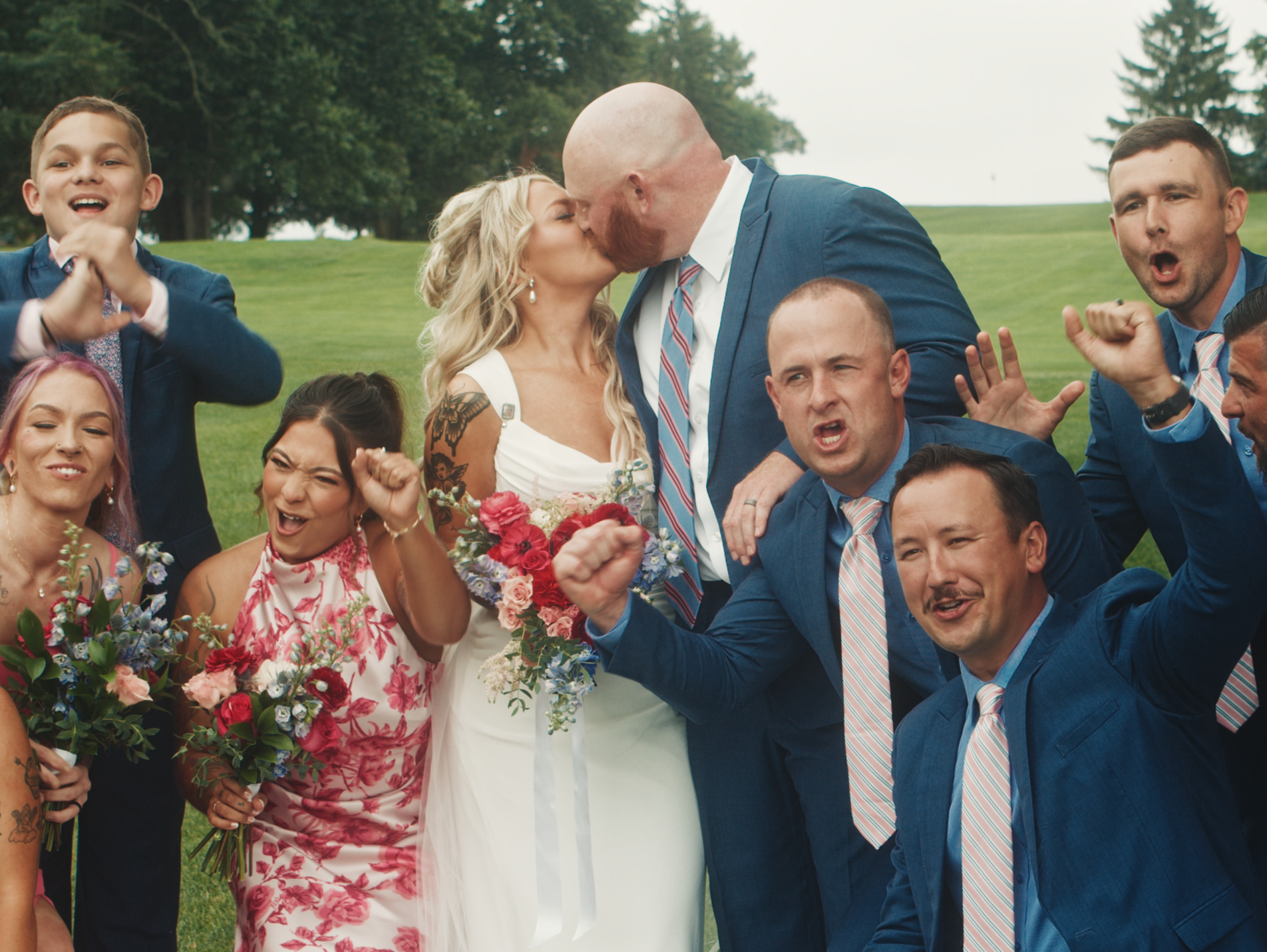 Couple kissing on golf course, surrounded by bridal party cheering.