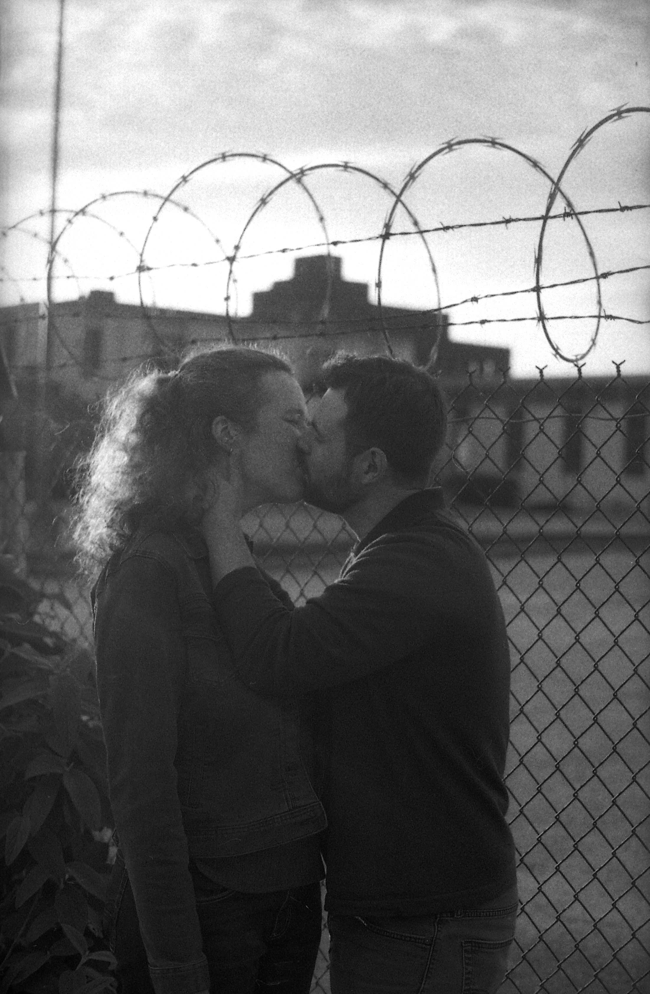 Couple kissing in front of razorwire fence, black and white.